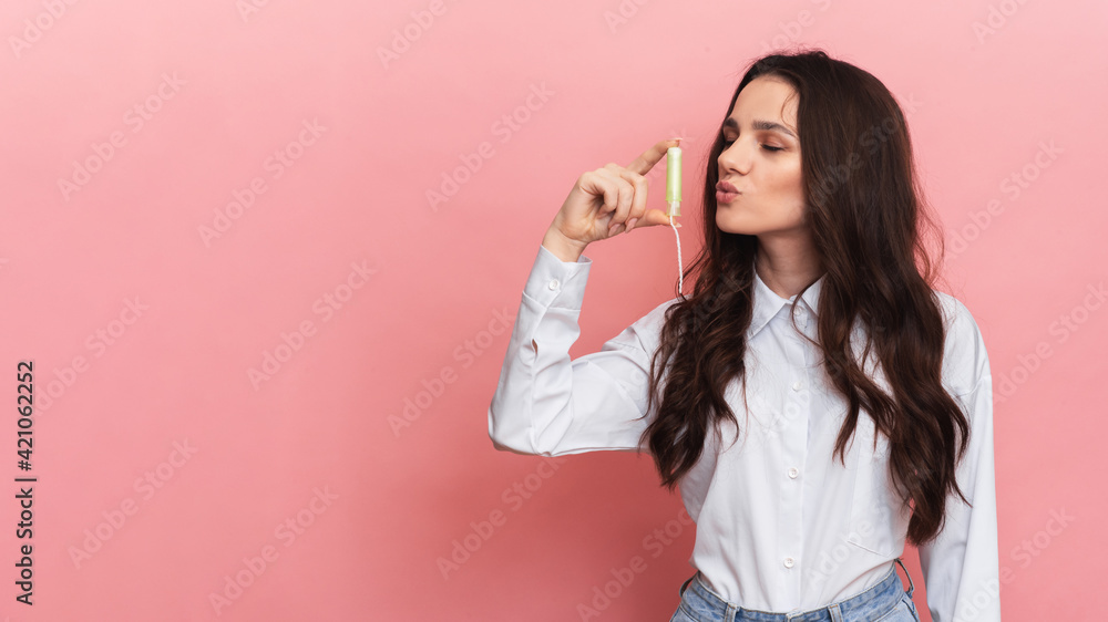 A young woman holds a menstrual swab with an applicator in her hands for easy use. Pink background. Space for text A young woman holds a menstrual swab with an applicator in her hands for easy use. Pink background. Space for text
