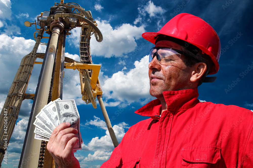 Well drilling worker with red hard hat holding US dollar bills on