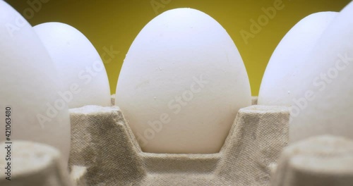 extreme close-up of white eggs in carton on yellow background.
