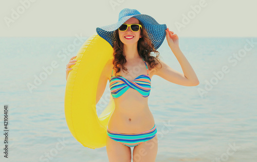 Summer portrait of happy smiling woman with inflatable circle wearing a straw hat on a beach, sea background