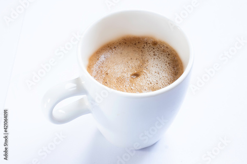 Cup of coffee with handle, isolated on a white table. Seen obliquely from above. Focus on the froth of the coffee. CUP WITHOUT SAUCER