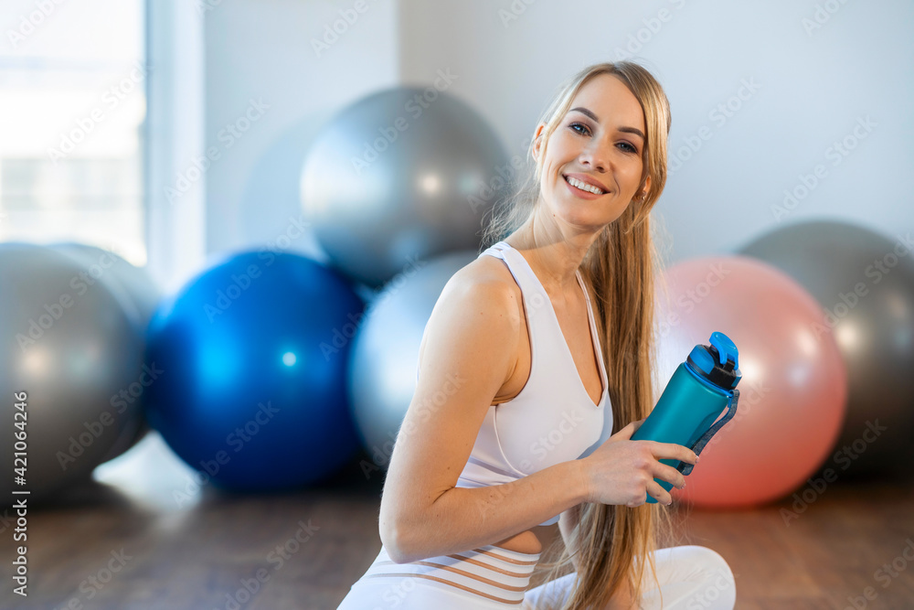 Portrait of beautiful fitness woman sitting on mat with sports bottle in her hands Portrait of beautiful fitness woman sitting on mat with sports bottle in her hands