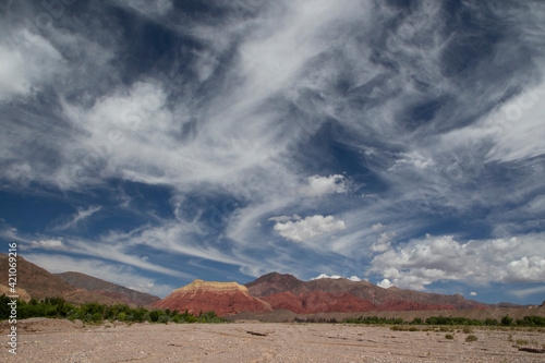 Desert background. View of the arid sand and colorful mountains under a dramatic blue sky with beautiful clouds. 