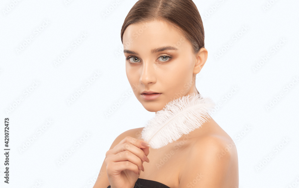 Portrait of a beautiful brunette girl with a white feather in her hand with healthy clean skin and fresh make-up. Aesthetic cosmetology and makeup concept. Portrait of a beautiful brunette girl with a white feather in her hand with healthy clean skin and fresh make-up. Aesthetic cosmetology and makeup concept.