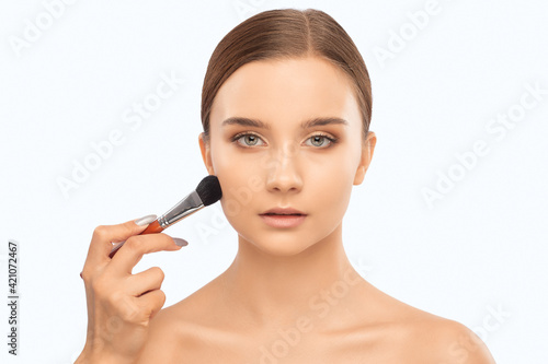 Portrait of a beautiful charming brunette girl with beautiful fresh makeup and healthy clean skin.Makeup artist holds a powder brush in her hands. Professional makeup concept