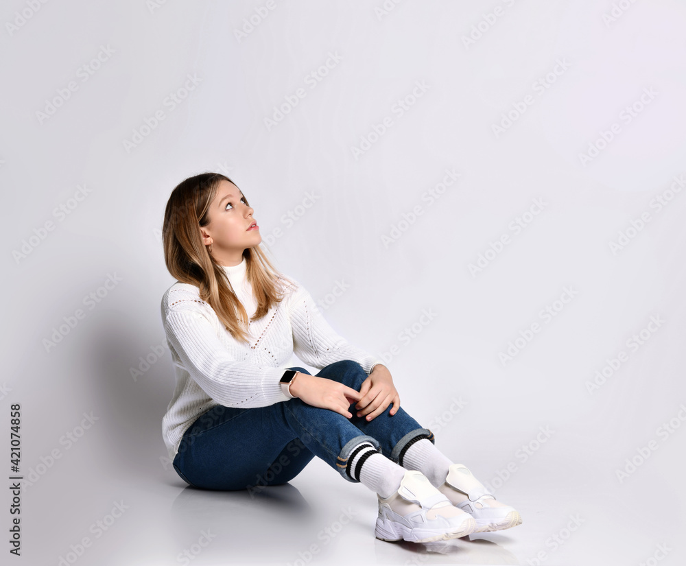 Cute teenage girl with long hair, smartwatch. Dressed in jeans, a sweater and sneakers. She is sitting on the floor and smiling, isolated on white. Cute teenage girl with long hair, smartwatch. Dressed in jeans, a sweater and sneakers. She is sitting on the floor and smiling, isolated on white.