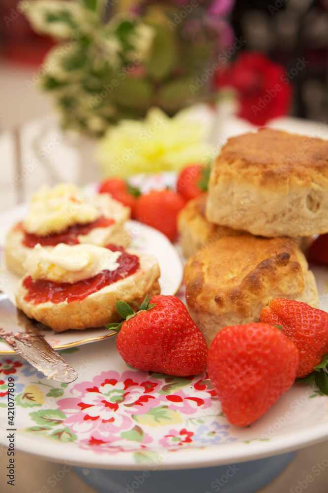 Scones on a floral plate with jam and cream with fresh strawberries. Flowers in the background Scones on a floral plate with jam and cream with fresh strawberries. Flowers in the background