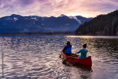 Couple friends canoeing on a wooden canoe during a colorful sunny sunset. Cloudy Sky Artistic Render. Taken in Harrison River  East of Vancouver  British Columbia  Canada.