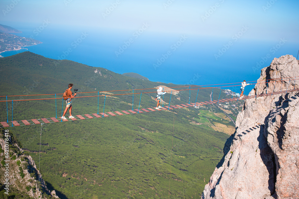 Family crossing the chasm on the rope bridge. Black sea background ...