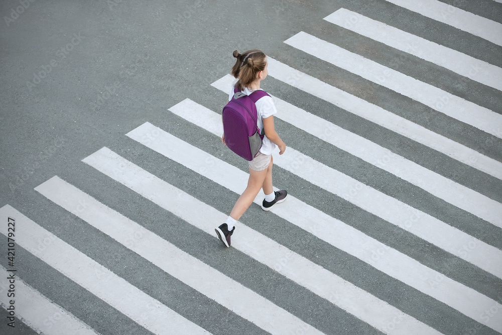 Schoolgirl crossing road on way to school. Zebra traffic walk way in the city. Concept pedestrians passing a crosswalk.  Stylish young teen girl walking with backpack. Active child.