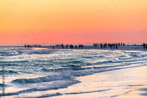 Siesta Key  Florida near Sarasota  USA at colorful sunset with coast gulf of mexico  silhouette of distant people in far distance on beach  waves washing
