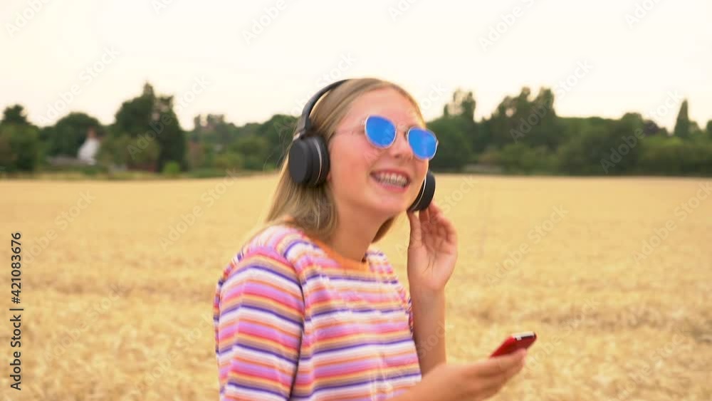 Slow motion tracking video clip of pretty blonde girl teenager young woman wearing a striped t- shirt and blue sunglasses walking listening to music on her cell phone and wireless headphones Slow motion tracking video clip of pretty blonde girl teenager young woman wearing a striped t- shirt and blue sunglasses walking listening to music on her cell phone and wireless headphones