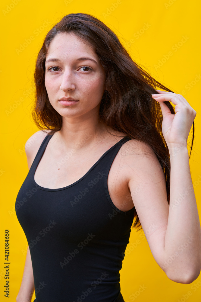 Vertical photo of a caucasian woman touching her hair and looking at camera, on yellow plain background Vertical photo of a caucasian woman touching her hair and looking at camera, on yellow plain background