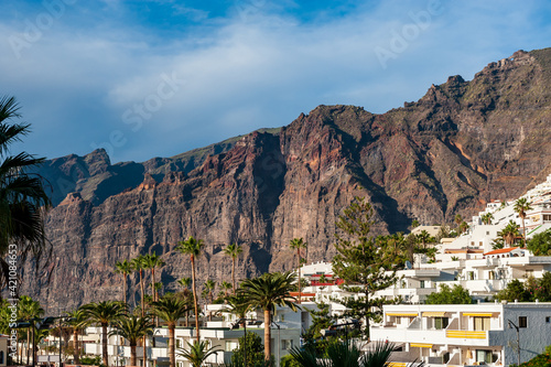 Los Gigantes village. Palm trees and white apartment houses in front of big rocks. Holiday destination near Pico del Teide mountain in El Teide National park. Tenerife, Canary Islands, Spain.
