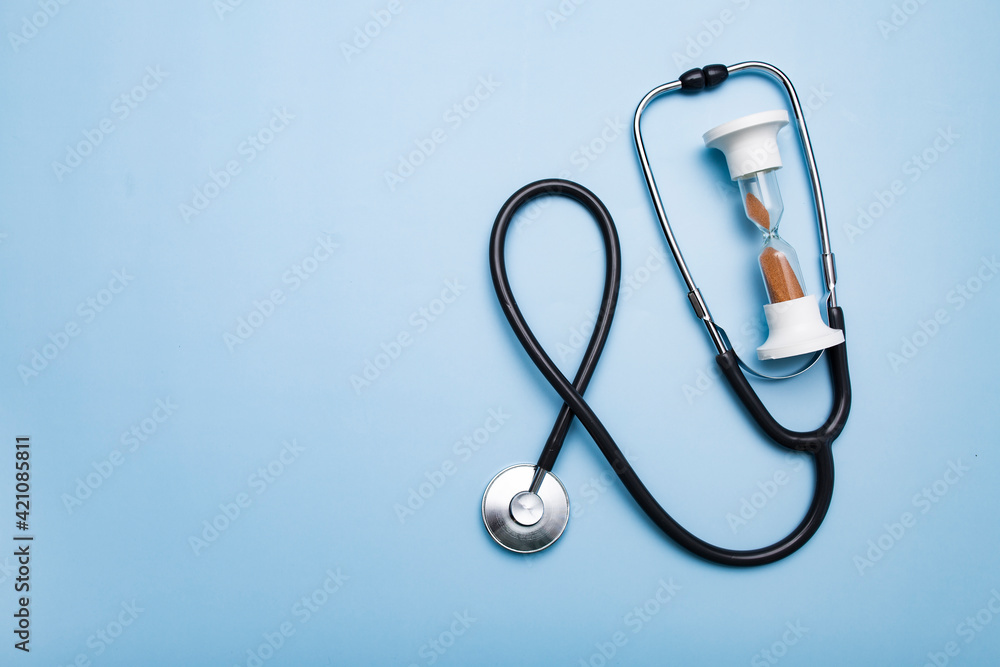 Stethoscope and hourglass on a blue background. Heart or breath check by doctor, missed elapsed time. Stethoscope and hourglass on a blue background. Heart or breath check by doctor, missed elapsed time.
