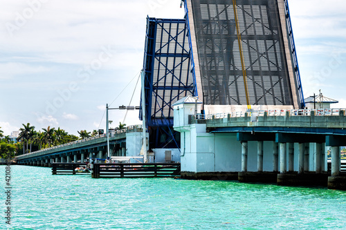 Opening drawbridge on Broad Causeway road at Bal Harbour of Miami, Florida with green turquoise ocean Biscayne Bay Intracoastal water with sail boat passing photo