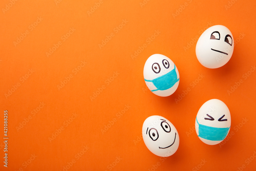 White Easter eggs in protective medical mask and two egg without mask on orange background. Easter on quarantine concept with place for text. Stop VIRUS COVID-19. Copy space. Egg in mask. White Easter eggs in protective medical mask and two egg without mask on orange background. Easter on quarantine concept with place for text. Stop VIRUS COVID-19. Copy space. Egg in mask.