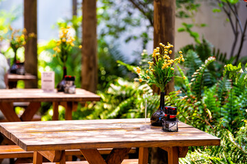 Wooden outside outdoor sitting restaurant empty area with picnic wooden tables chairs bench in patio terrace garden with green plants in Florida with flower bouquet and condiments