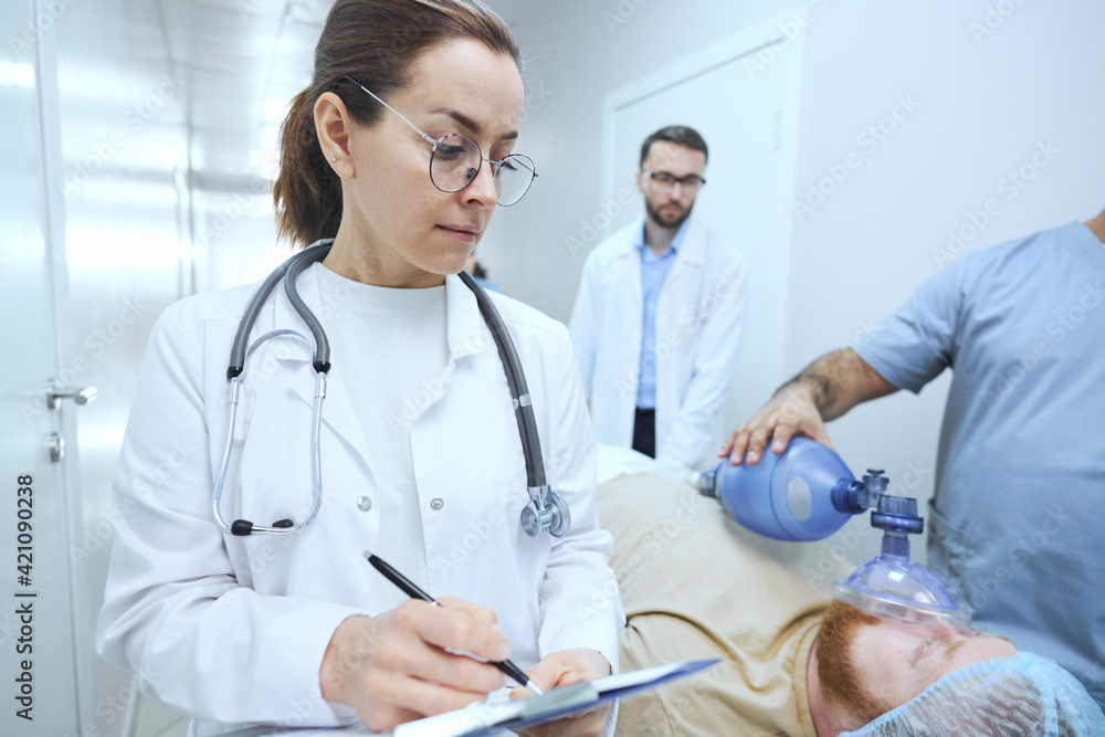 Female doctor in white coat filling the medical card of the patient who unconscious at hospital Female doctor in white coat filling the medical card of the patient who unconscious at hospital
