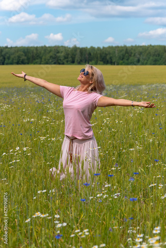 Fototapeta Naklejka Na Ścianę i Meble -  A middle-aged woman in a field of flowers, enjoying the summer, rejoicing in the sun. 