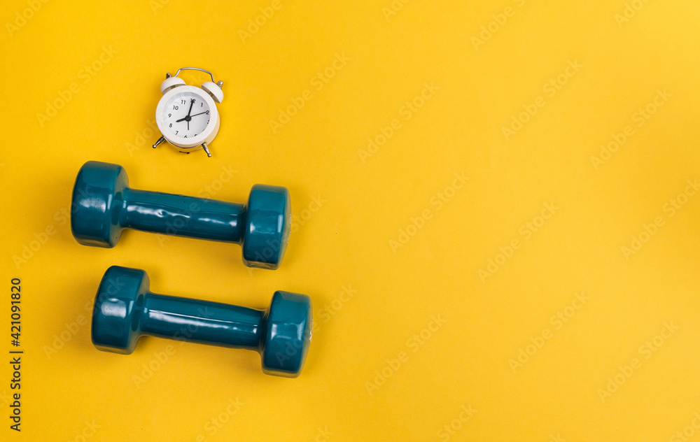 Dumbbell, alarm clock on yellow background. Minimalistic sport concept. Top view. - obrazy, fototapety, plakaty 