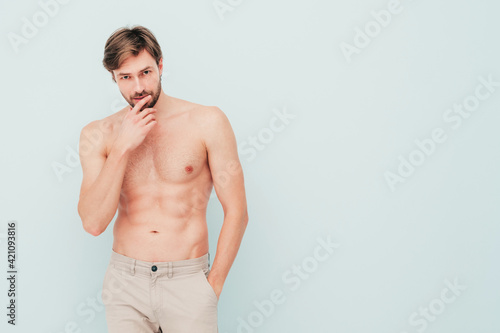 Portrait of sporty handsome strong man. Healthy smiling athletic fitness model posing near light blue wall. Confident sexy fashion male with naked nude torso. Lambersexual in studio