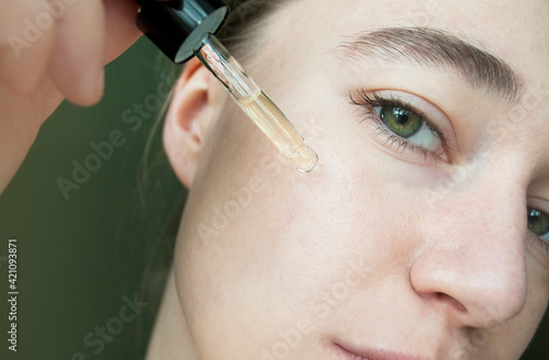 Portrait of a woman applying liquid from a glass bottle, skin texture. Apply a moisturizing tea tree serum to your face. photo