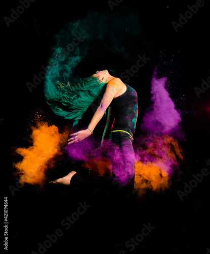 A young woman makes a high jump with explosion of dry colorful holi powder. Holi festival india