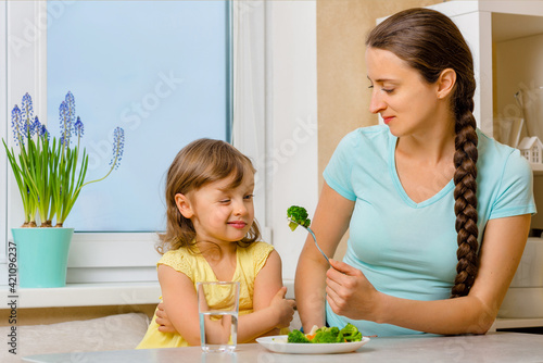 The kid is skeptical about broccoli and does not want to eat it. Organic cabbage and food. Mother tries to feed the girl