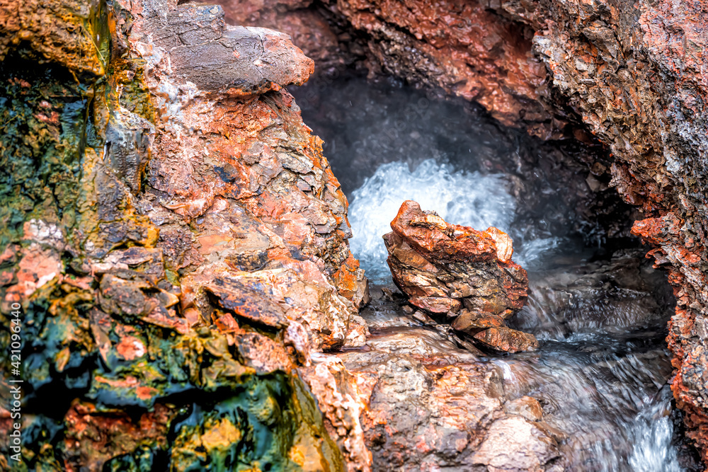 Closeup of steam geyser in Deildartunguhver hot springs in Iceland with red rock colorful cave opening hole and water boiling
