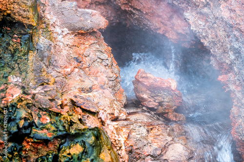 Closeup of steam geyser long exposure steam in Deildartunguhver hot springs in Iceland with red rock colorful cave opening hole and water boiling