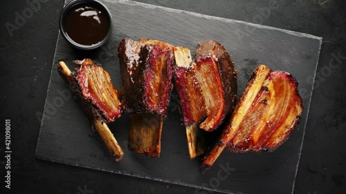 Smoked beef ribs on a black slate board, top view, rotating around its axis. Smoked beef meat with bone on a black background.