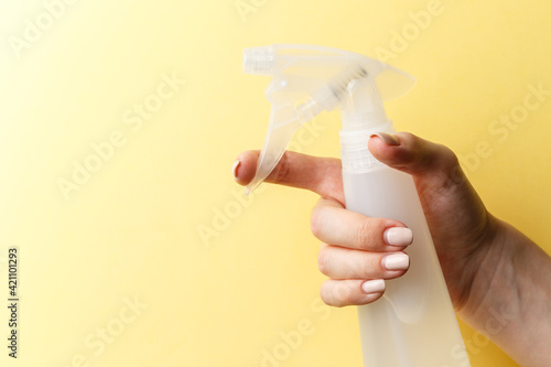 A woman's hand holds a spray bottle on bright yellow background. Natural products for cleaning or body care concept. Close-up
