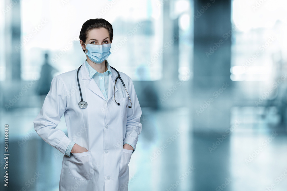 A medical professional in a mask stands . A medical professional in a mask stands .