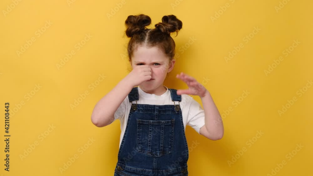 Portrait of unhappy little preschool girl kid feeling bad and dislike smell and hold nose from funny odor, wears white t-shirt, isolated on yellow studio background, six year child looking at camera Portrait of unhappy little preschool girl kid feeling bad and dislike smell and hold nose from funny odor, wears white t-shirt, isolated on yellow studio background, six year child looking at camera
