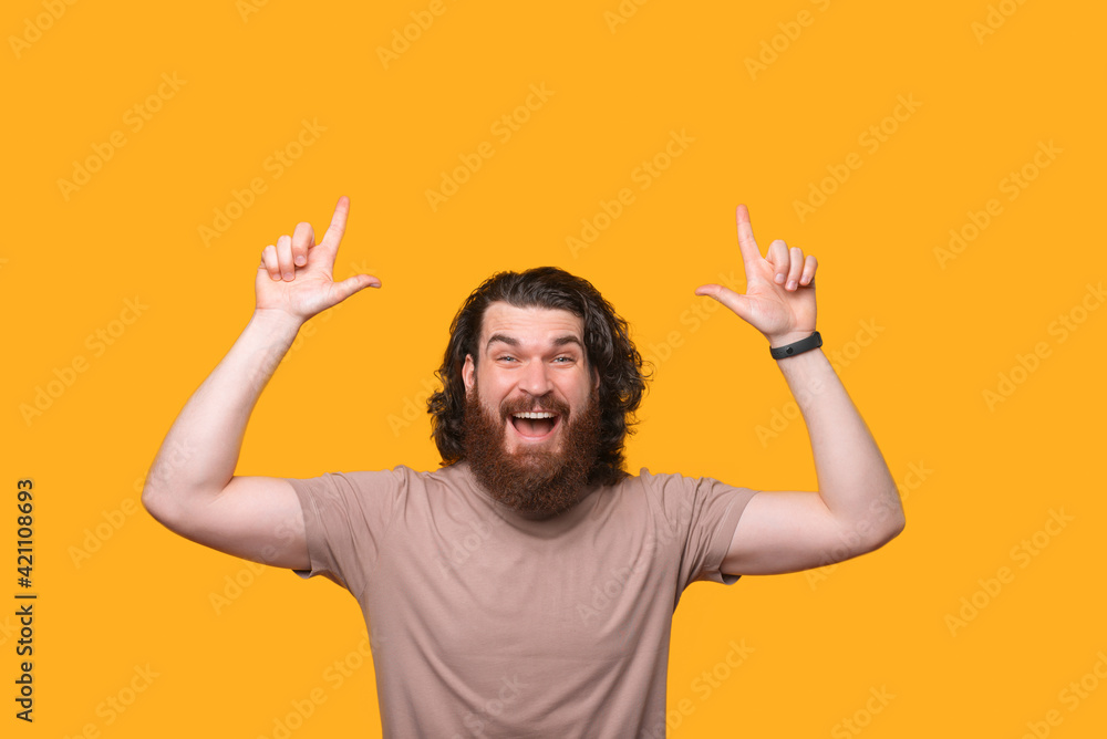 Handsome young bearded man with curly hair pointing up over yellow background Handsome young bearded man with curly hair pointing up over yellow background
