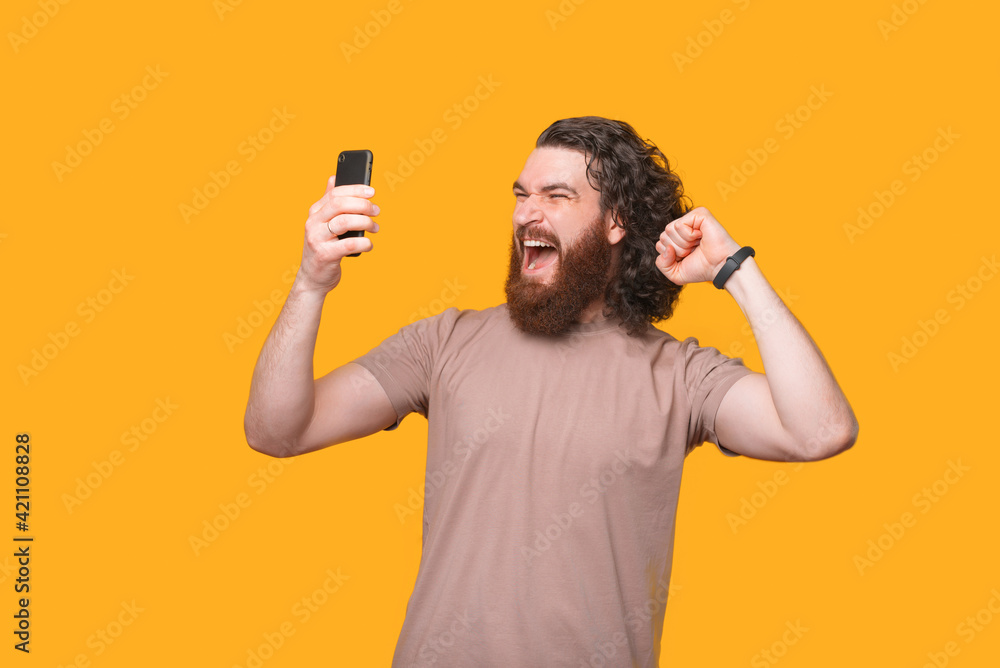 Amazed screaming bearded hipster man celebrating success and looking at smartphone, supporting favorite team Amazed screaming bearded hipster man celebrating success and looking at smartphone, supporting favorite team
