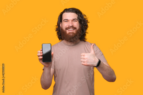 This is a good choice, smiling bearded hipster man showing thumb up and smartphone