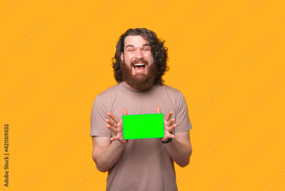 Excited young bearded man with long curly hair showing green screen on tablet Excited young bearded man with long curly hair showing green screen on tablet