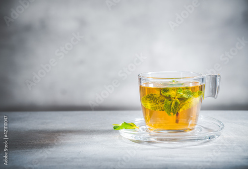 Mint tea with leaves in glass cup on gray background, front view