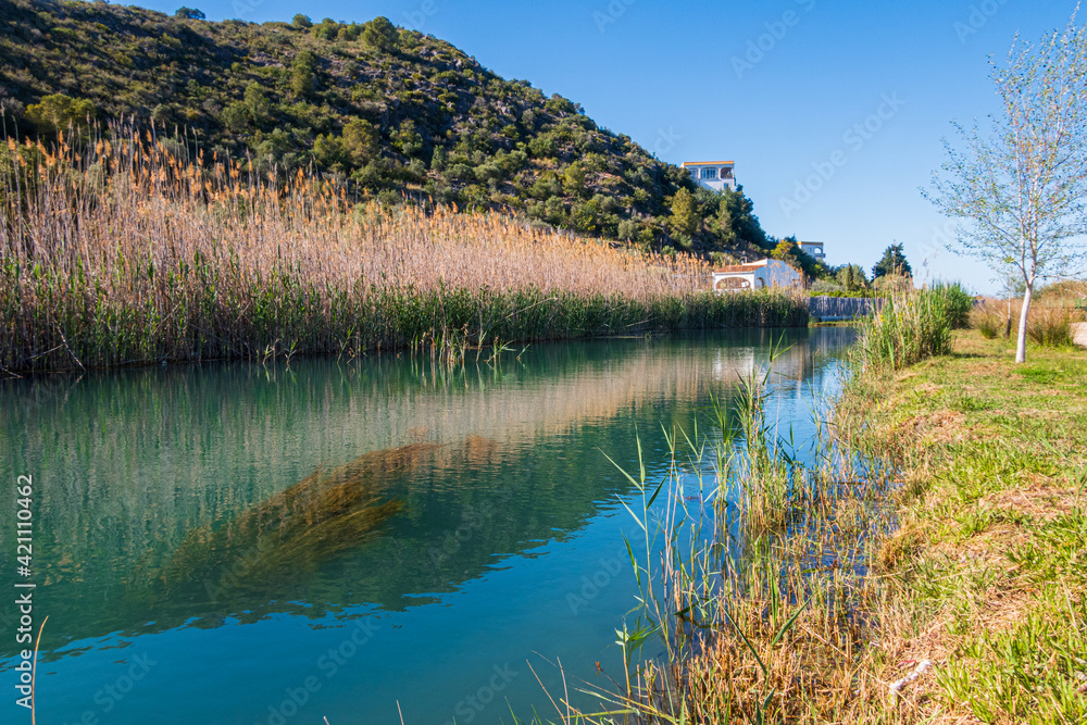 River crossing a marsh with reeds, and some mountains in the background, with a blue and clean sky. In Oliva (Valencia, Spain). River crossing a marsh with reeds, and some mountains in the background, with a blue and clean sky. In Oliva (Valencia, Spain).