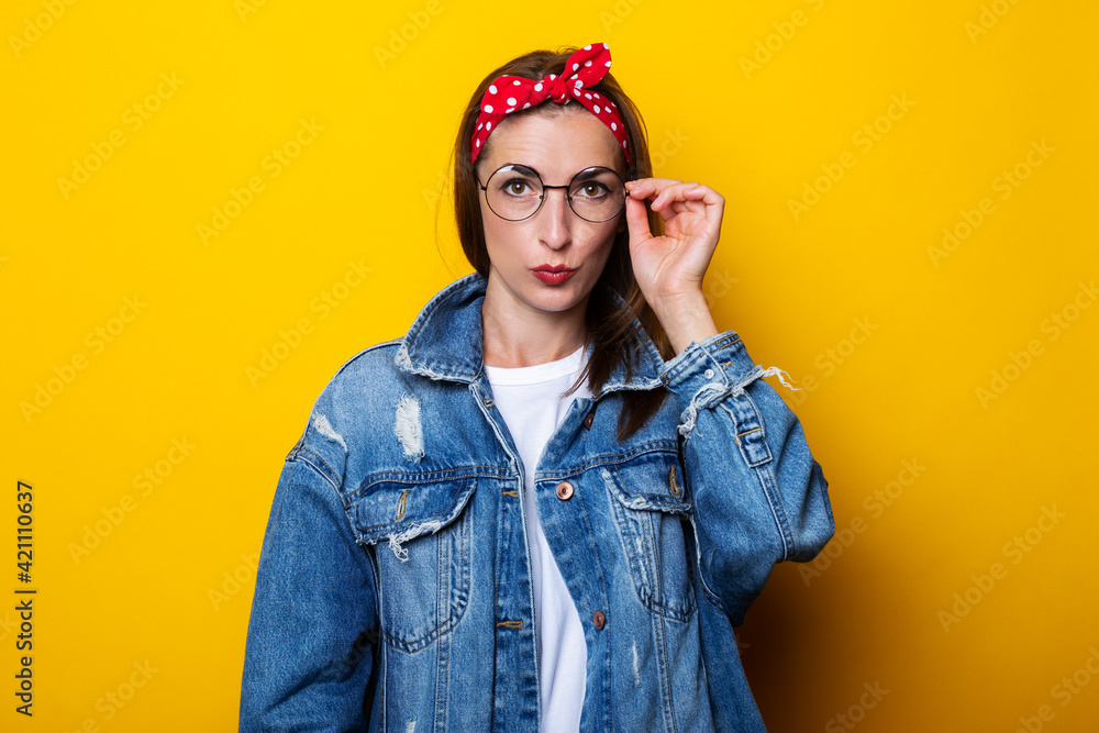 Serious young woman in hair band, in denim jacket with glasses on yellow background. Serious young woman in hair band, in denim jacket with glasses on yellow background.
