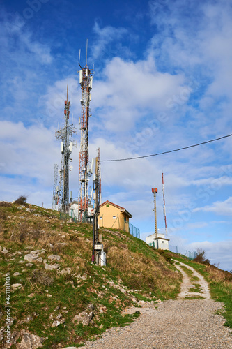 Two towers of communications with antennas against deep blue sky and white clouds