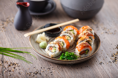 Sushi maki rolls with salmon, eel, avocado, cucumber on a plate with chopsticks, soy sauce, wasabi and ginger. Japanese traditional fish food closeup served for lunch in modern gourmet restaurant