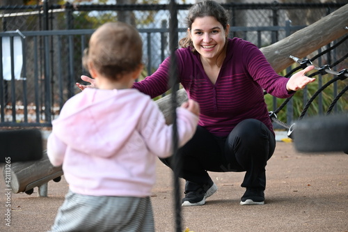A mother playing at the park waiting for her child to run to her open arms