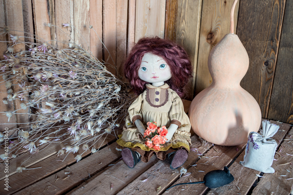 Fototapeta premium A textile interior doll sits on a wooden background with a pumpkin, dried flowers and a mouse.
