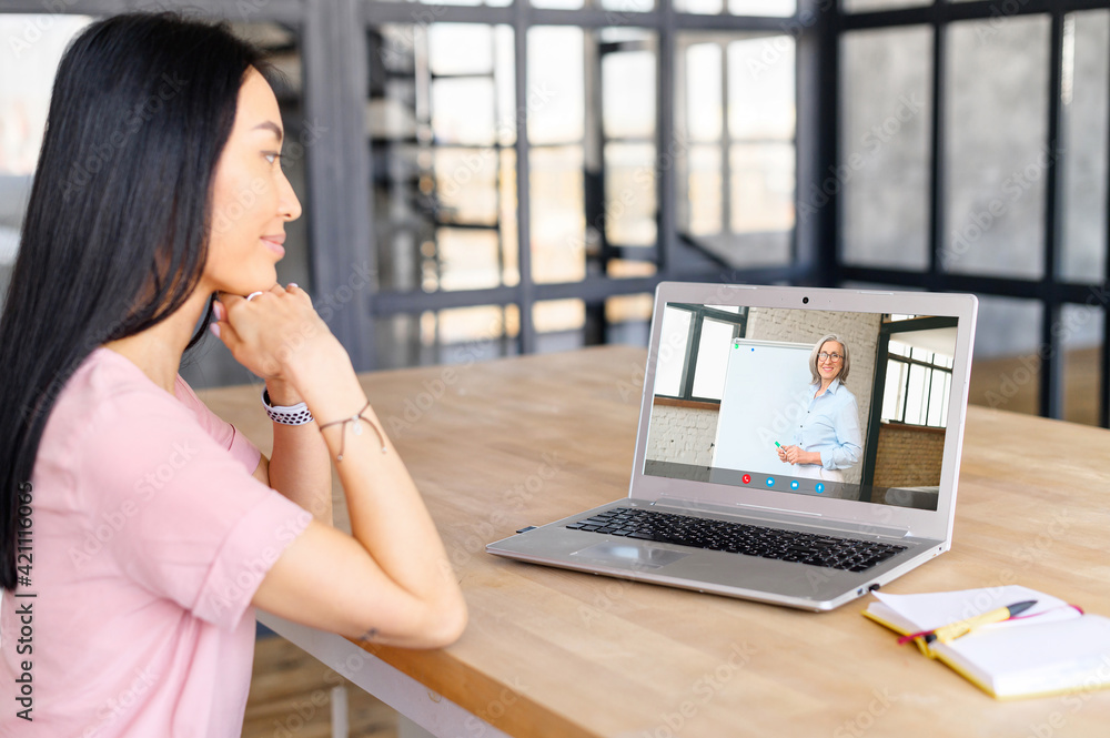 Attentive Asian woman using app for studying online via laptop, taking virtual course, actively listening to the lecturer, studying from home, old lady teacher explaining material on whiteboard Attentive Asian woman using app for studying online via laptop, taking virtual course, actively listening to the lecturer, studying from home, old lady teacher explaining material on whiteboard