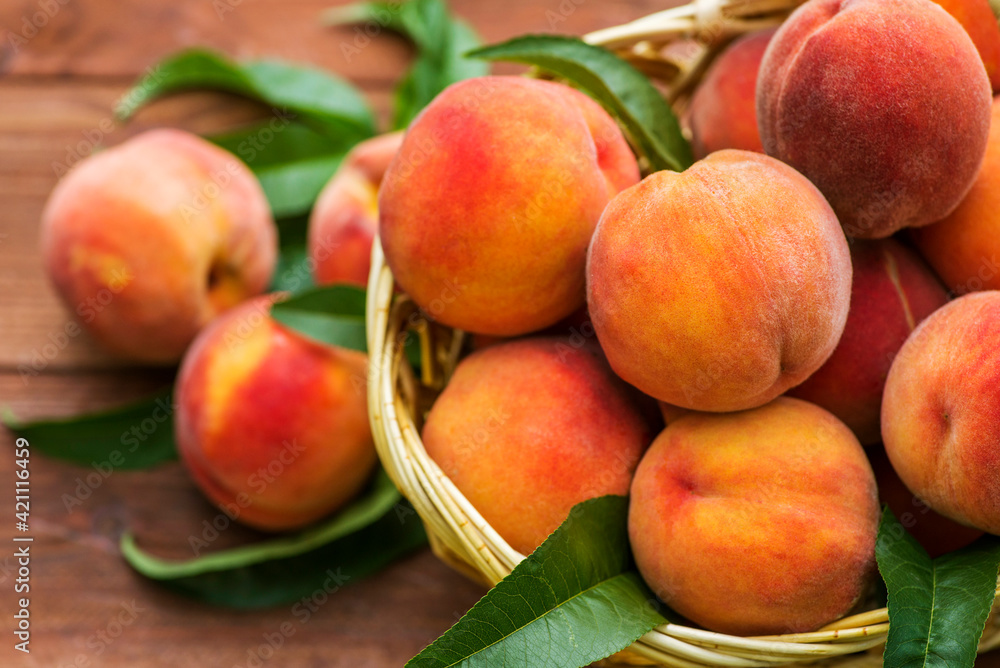 Fresh juicy peaches with leaves in a wicker basket on a wooden background. Freshlypicked peaches in a wicker basket Fresh juicy peaches with leaves in a wicker basket on a wooden background. Freshlypicked peaches in a wicker basket