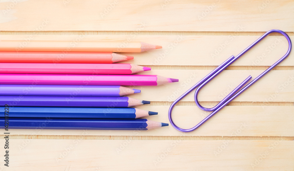 Fototapeta premium Composition with pink, purple and blue pencils and clip on wood background, top view
