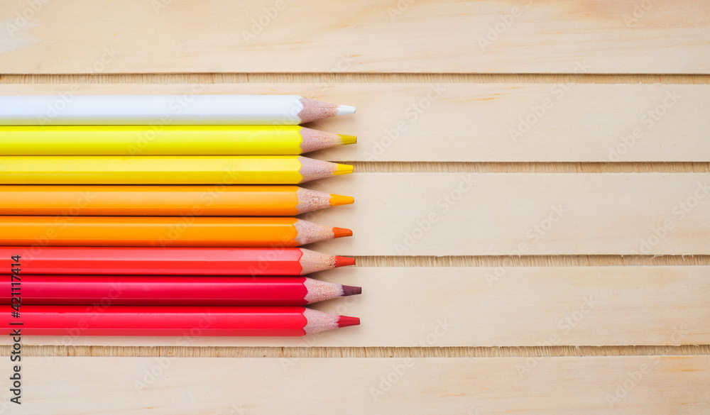 Composition with white, yellow, orange, red pencils on wood background, top view Composition with white, yellow, orange, red pencils on wood background, top view